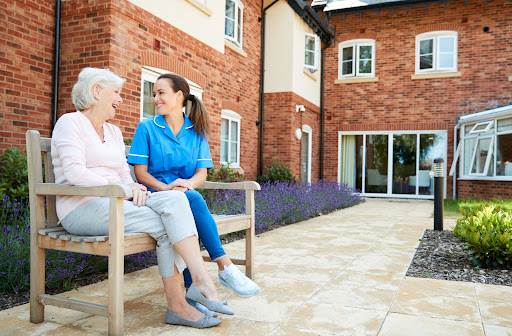 A female nurse sitting outside on a bench with an assisted living patient