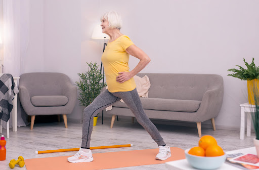a senior woman does a standing lunge on a yoga mat