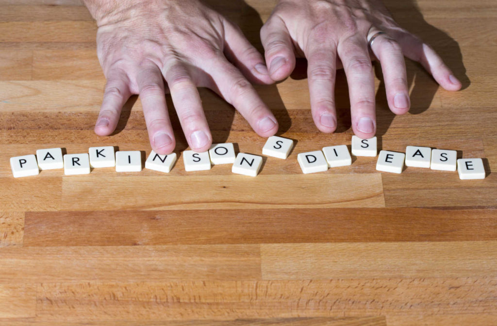 A seniors hands placed above block letters on a table spelling out parkinsons disease.