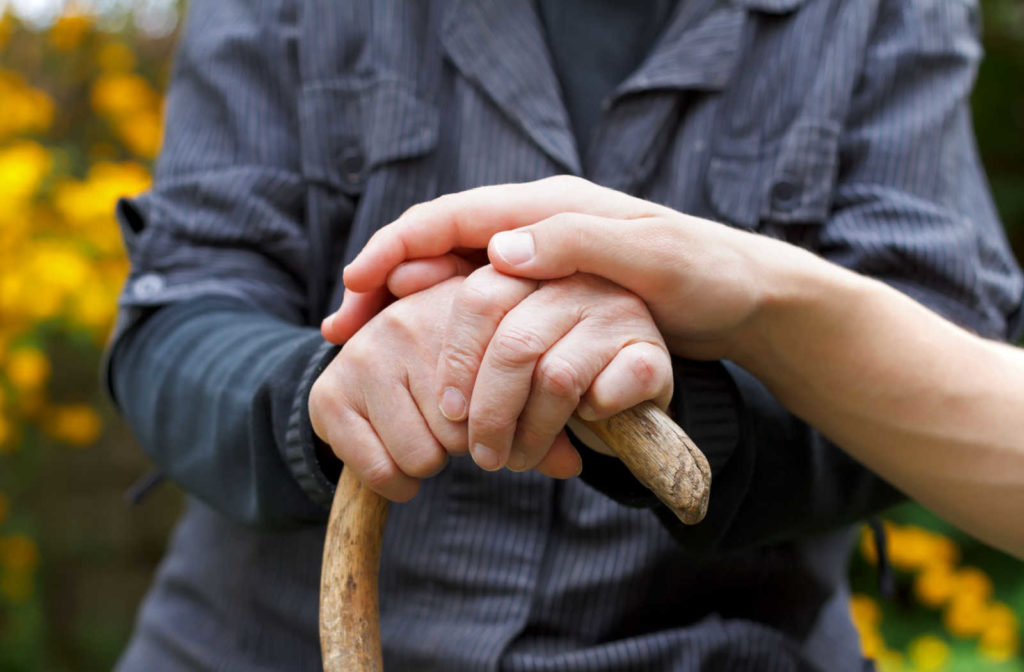A senior holding a can with a caregiver's hand placed on top.