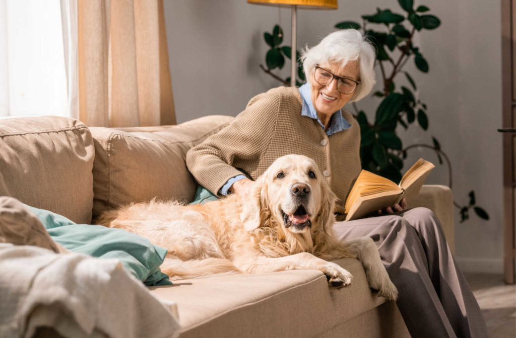 A senior woman sitting on a couch with a dog beside her.