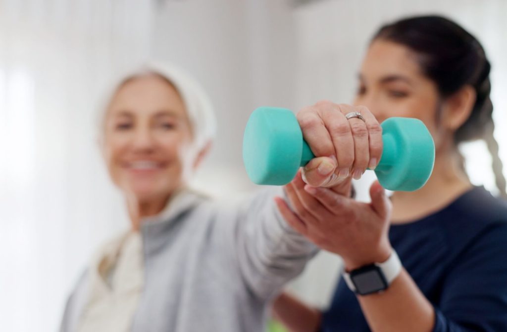 An older woman lifting weights with assistance from a trainer.