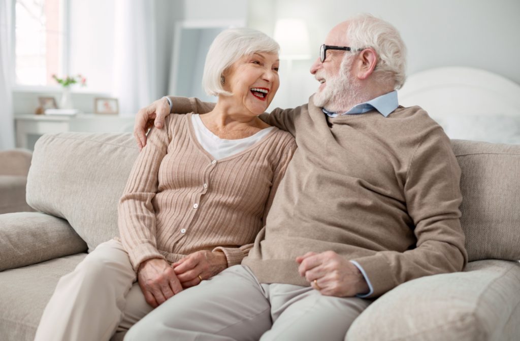 A senior couple embraces on the couch inside their independent living apartment.