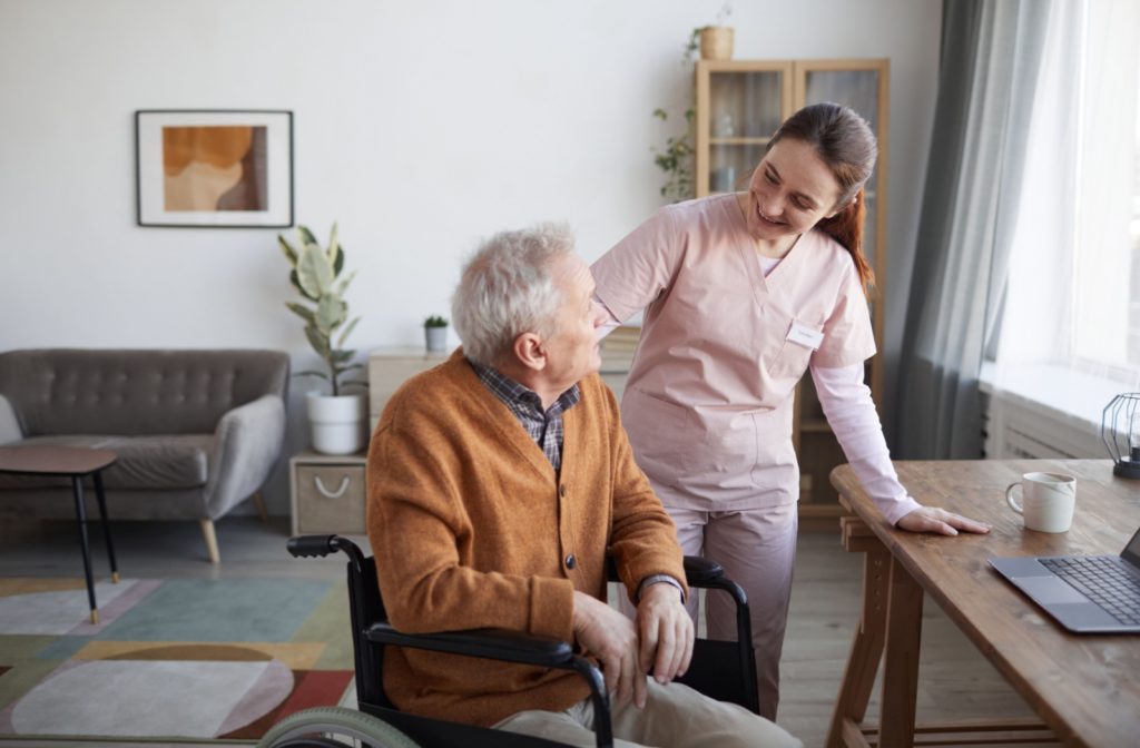 A smiling caregiver in assisted living visits a resident in his wheelchair.