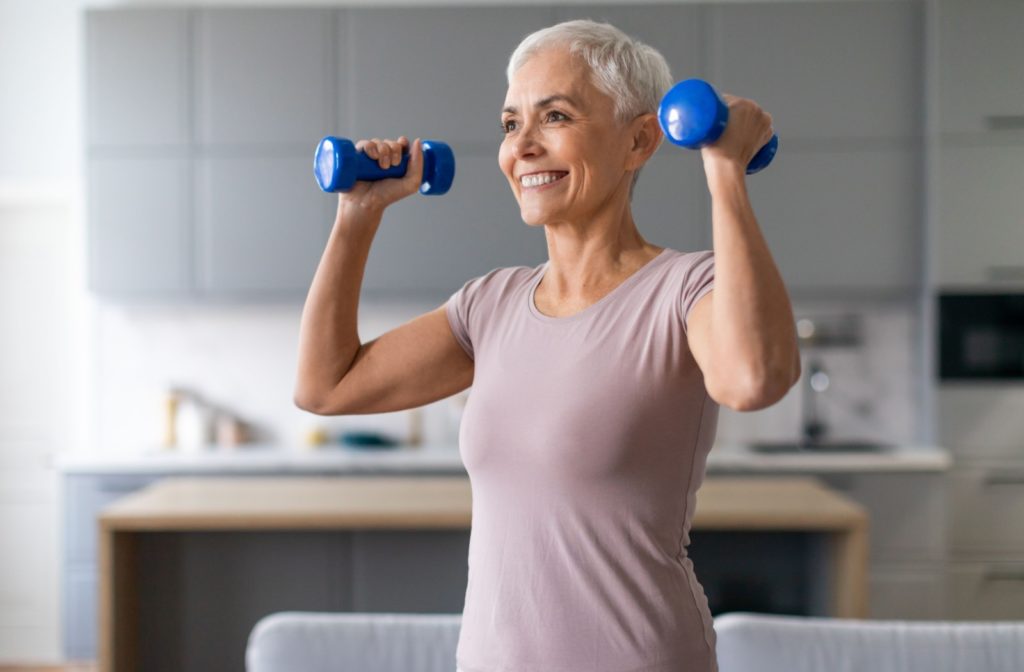 An older adult performing a strength exercise with dumbbells, lifting them at shoulder level while smiling.