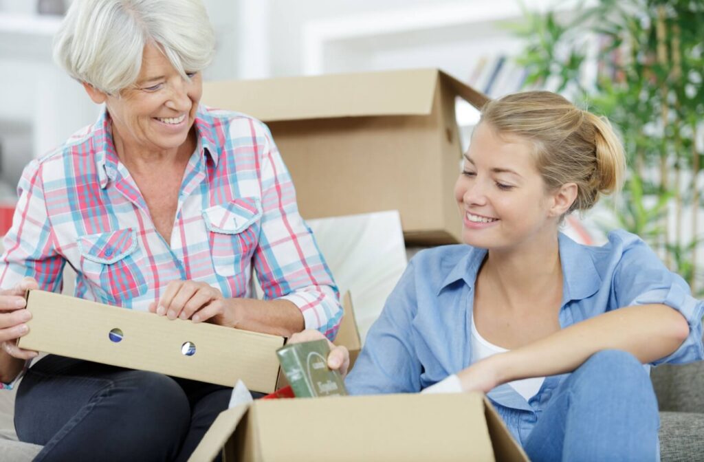 An older adult smiling at their adult child while packing a box of books together during a move to independent living.