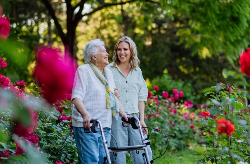 A senior uses a walker to enjoy the outdoor garden with an adult child during a visit to their senior living community