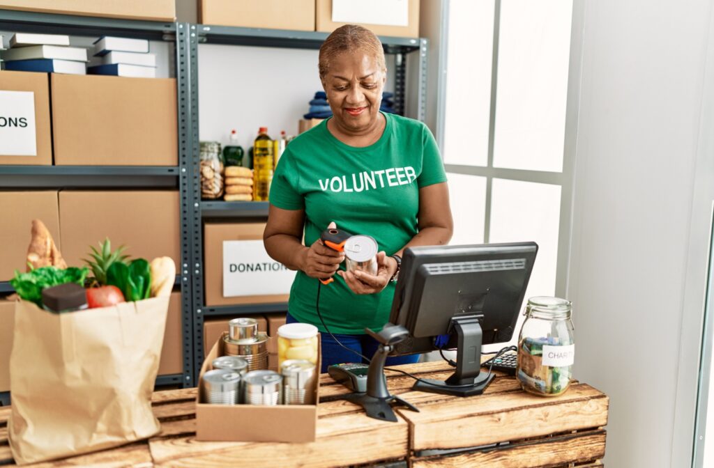 A senior wearing a green volunteer shirt helps organize donations at a local food bank to give back to their community.