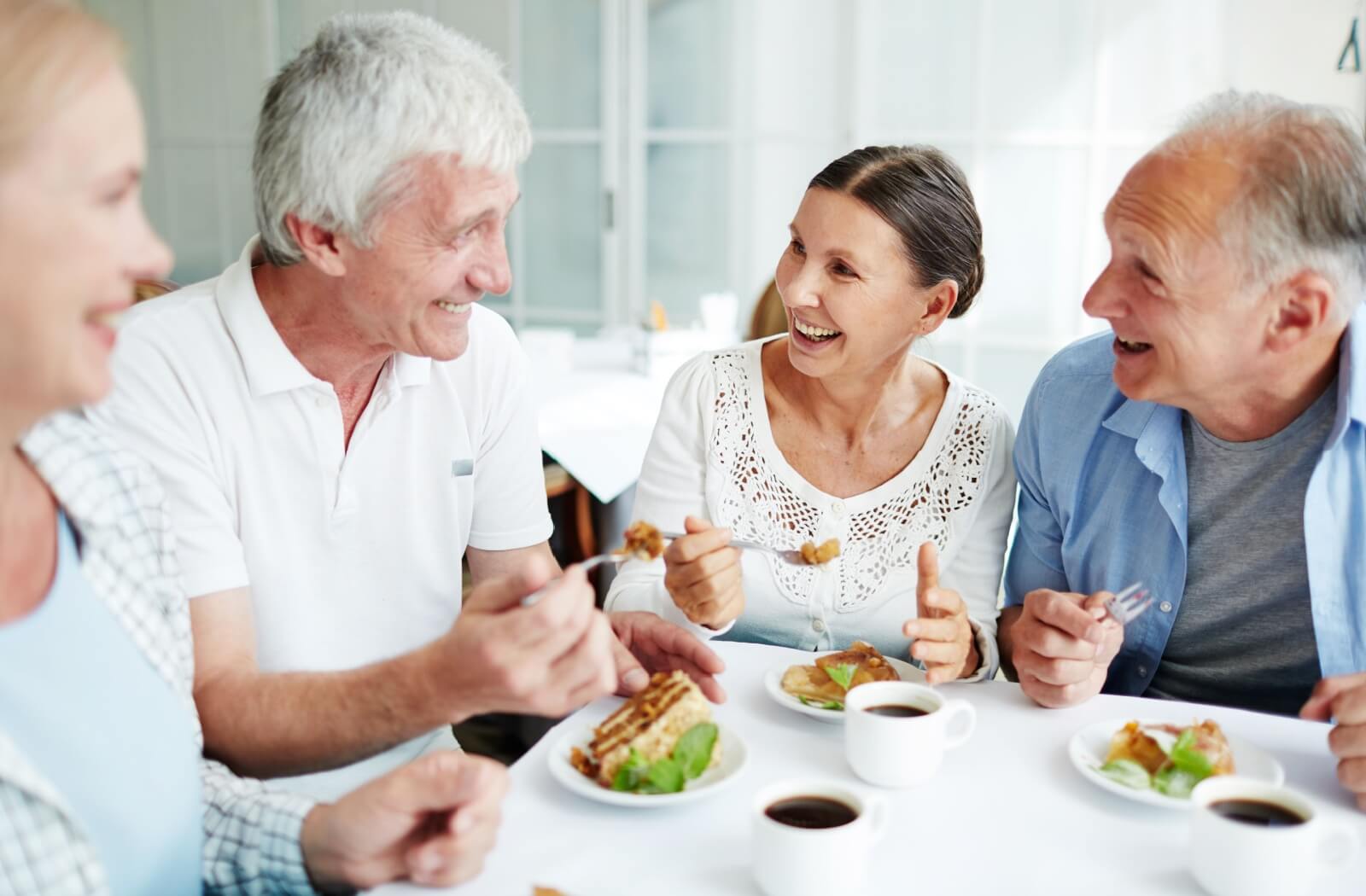 Four seniors laughing together over a conversation while sharing lunch in their senior living community
